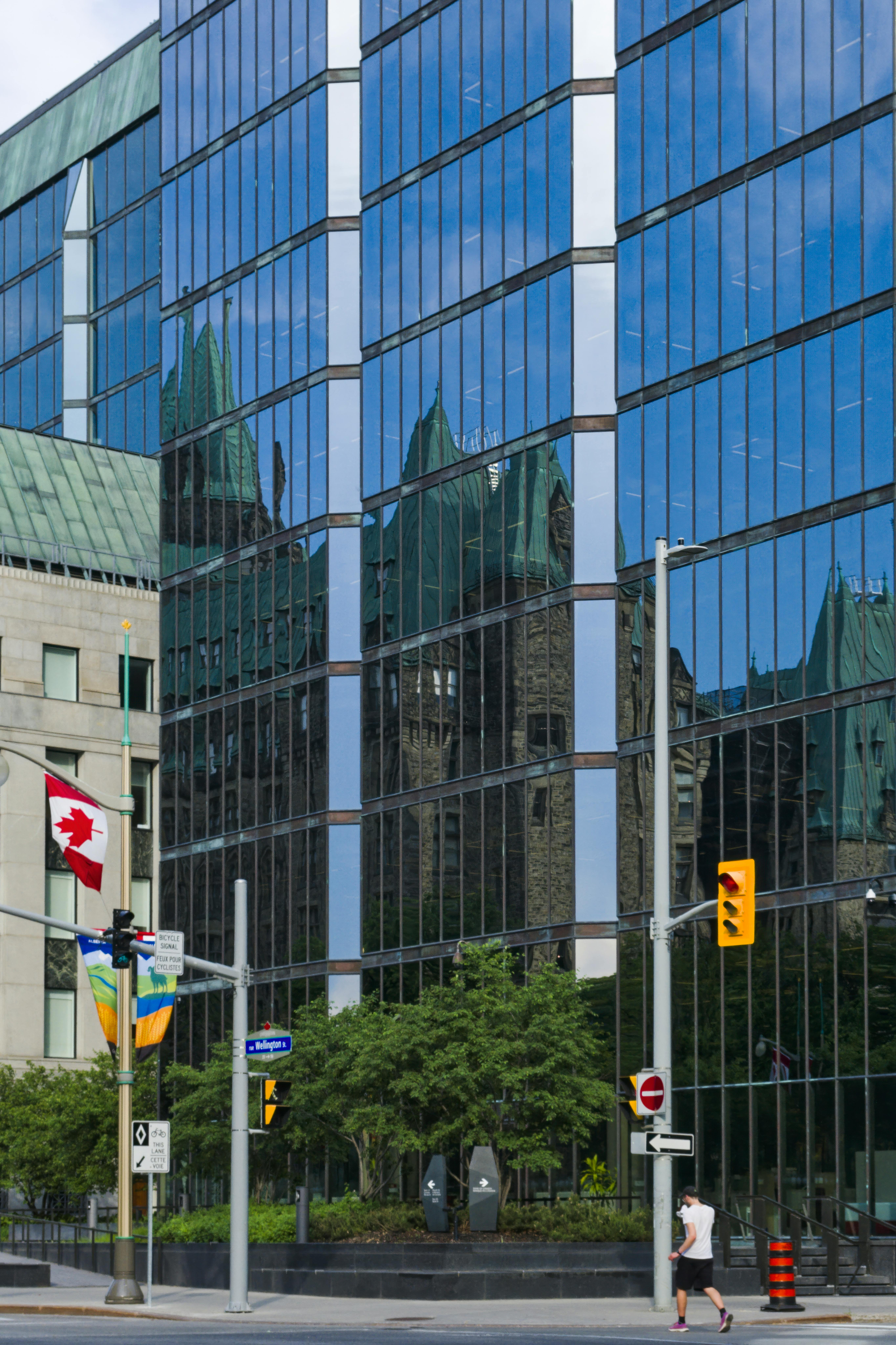 Édifice de bureaux au centre-ville d'Ottawa reflétant les tours du Parlement, drapeau canadien au premier plan